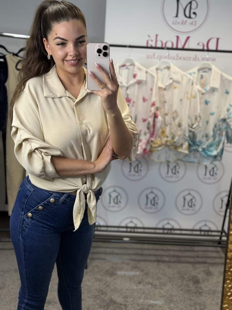 Női modell egy bézs női ingben, tükörben selfie-t készít.