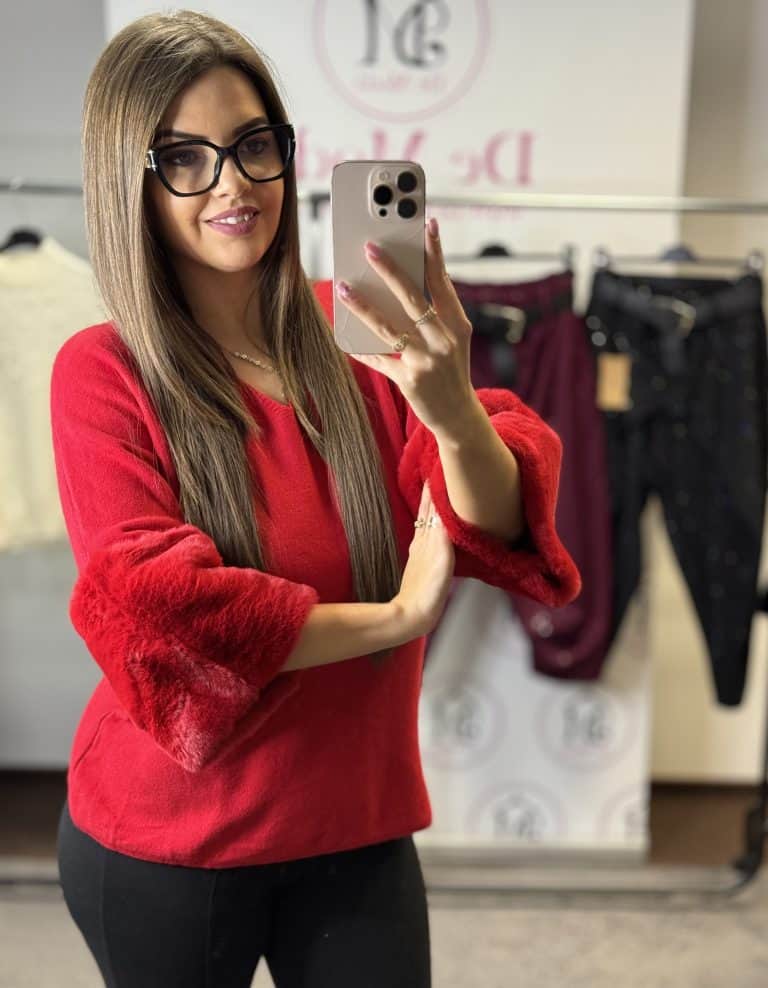 Női modell piros kötött felsőt visel, szőrmés ujjal, fényképez selfie-t a boltban.