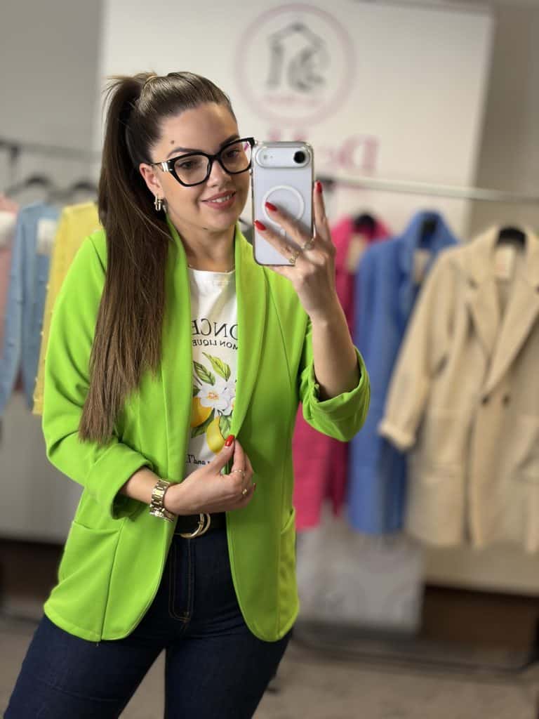 Női modell neonzöld blézert visel, fényképez selfie-t egy ruházati boltban.