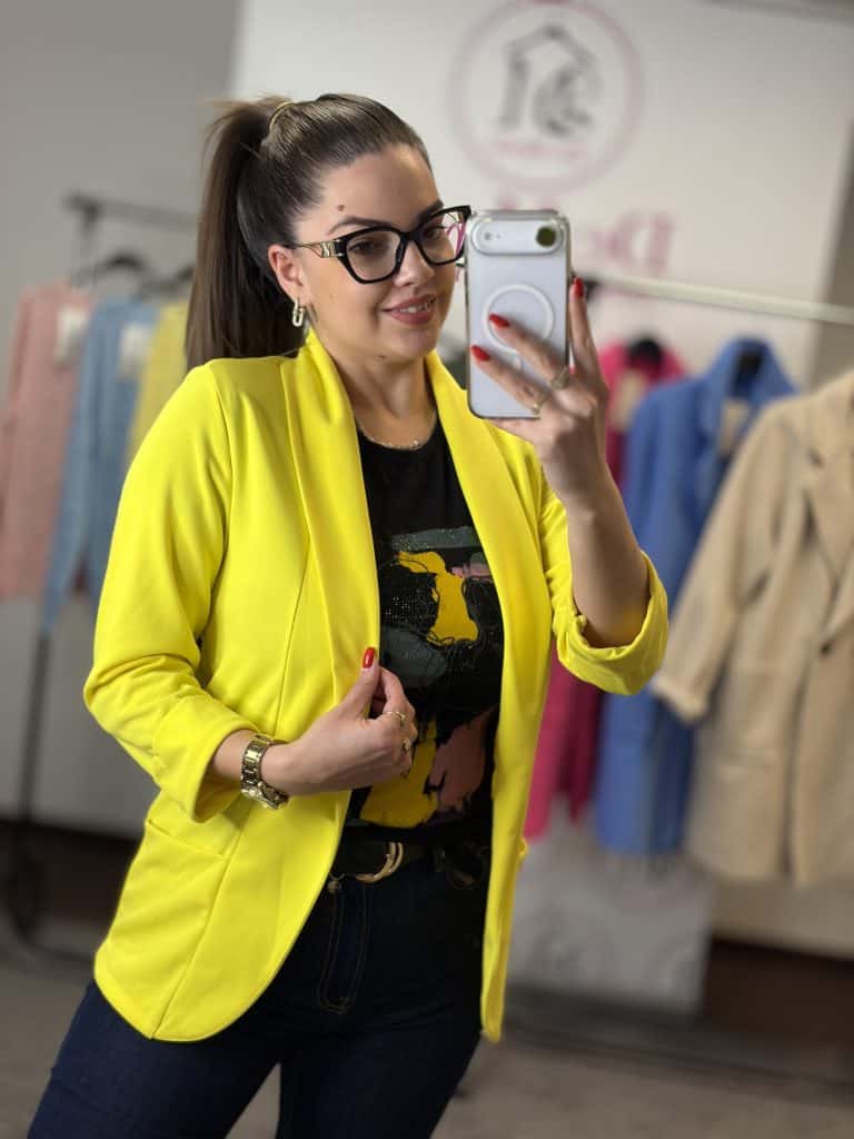 Női modell citromsárga blézert visel, fényképez selfie-t a ruházati boltban.