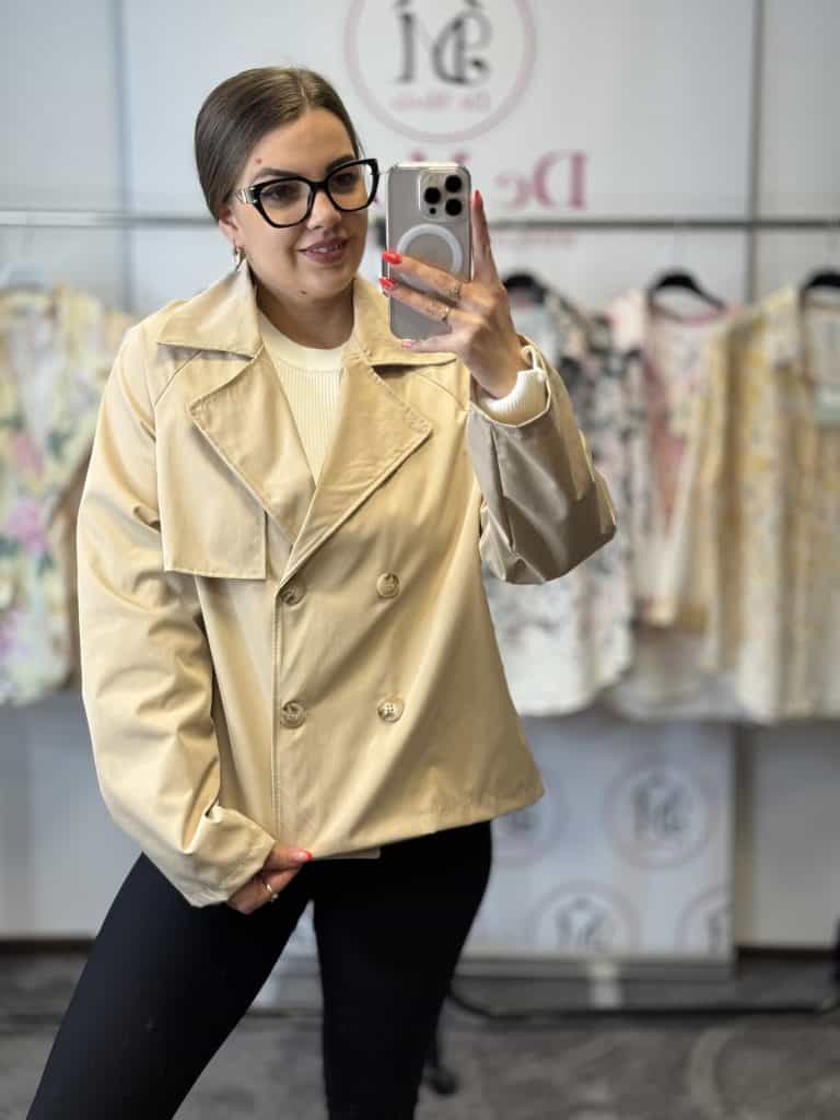 Női modell bézs színű, rövid fazonú ballonkabátot visel, fényképez selfie-t.