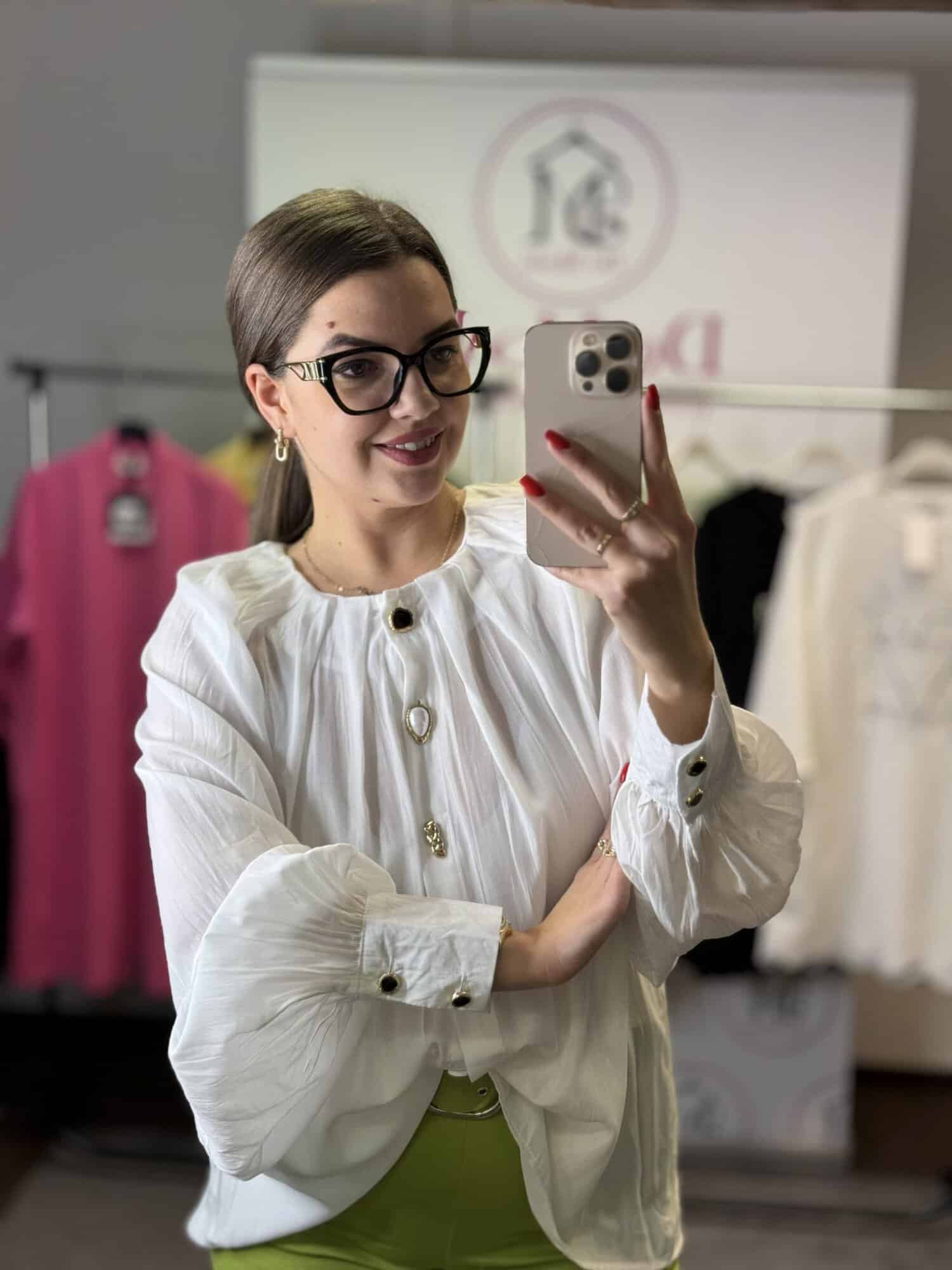 Női modell fehér, bő fazonú inget visel, szemből selfie-t készít.