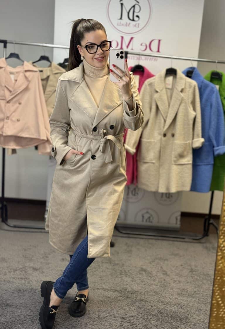 Női modell bézs színű hosszú trench coat próbál a divatüzletben.